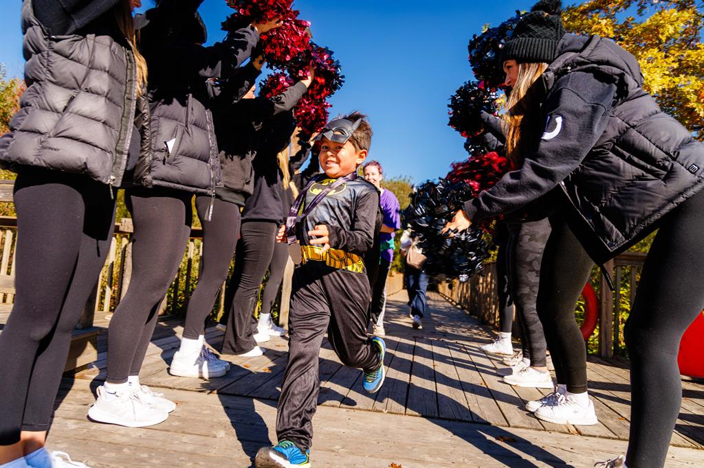 Child in batman costume passes by cheerleaders